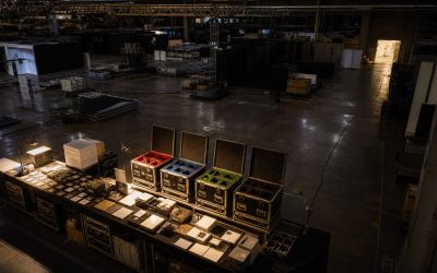 閉場後の展示会場で名刺・資料・関心テーマを4種類のフォローケースへ整理し、遠くの明るい業務入口へつなぐことで、展示会後のWeb案内と営業連携を示す夜間撤収現場